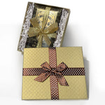 Load image into Gallery viewer, An image of a gold gift box with brown ribbon with white dots, opened with a package of chocolate bars inside surrounded by crinkle paper.
